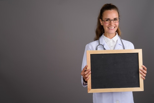 Doctor hermoso joven de la mujer contra fondo gris