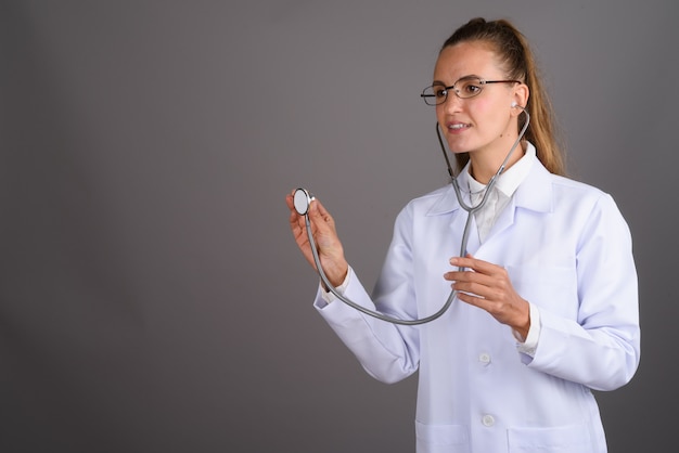 Doctor hermoso joven de la mujer contra fondo gris