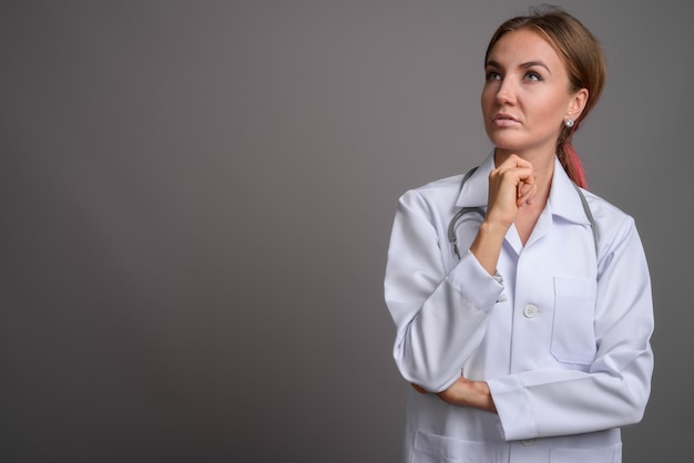 Doctor hermoso joven de la mujer contra la pared gris