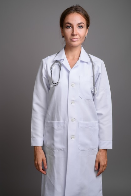 Doctor hermoso joven de la mujer contra la pared gris