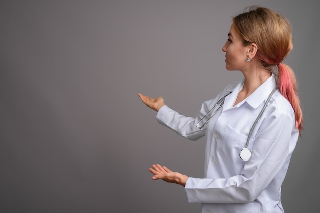 Doctor hermoso joven de la mujer contra la pared gris