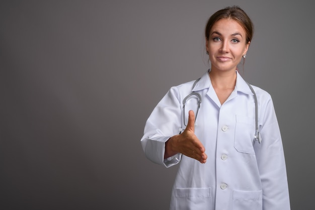 Doctor hermoso joven de la mujer contra la pared gris