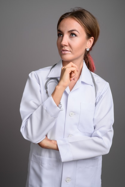 Doctor hermoso joven de la mujer contra la pared gris