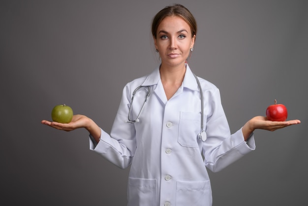 Doctor hermoso joven de la mujer contra la pared gris