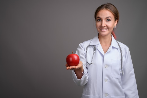 Doctor hermoso joven de la mujer contra la pared gris