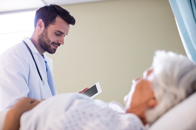 Foto doctor hombre discutiendo informe médico sobre tableta digital con paciente senior femenino en la sala