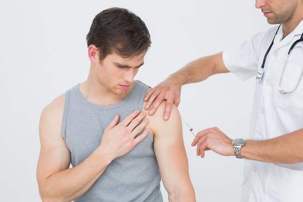 Doctor hombre inyectando un brazo de pacientes masculinos jóvenes