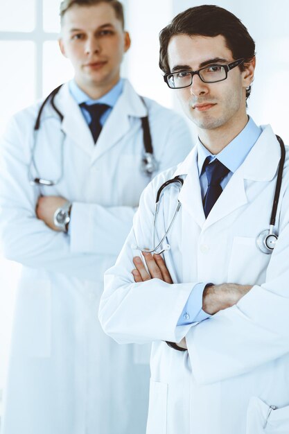 Doctor hombre de pie derecho con un colega en el fondo. Grupo de médicos. Perfecto servicio médico en clínica. Conceptos de medicina y salud.
