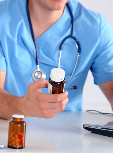 Doctor hombre sentado en la mesa y sosteniendo la botella