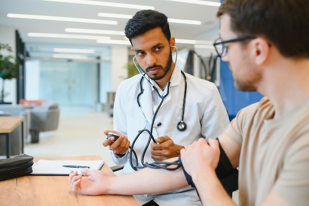 Doctor indio sosteniendo un dial mientras mide la presión arterial del hombre