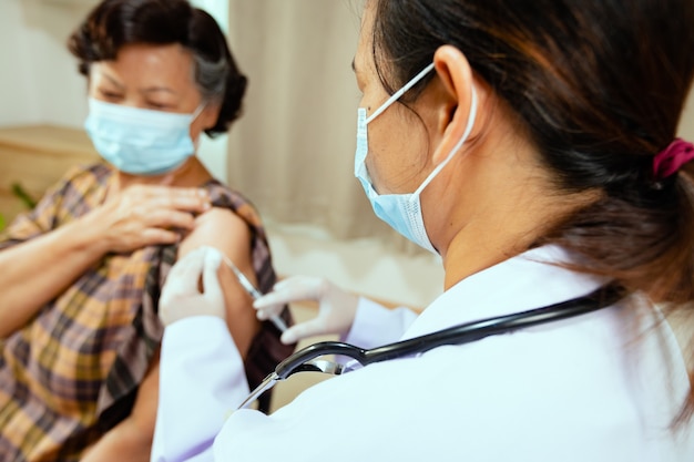 Doctor inyectando vacunación en el brazo de la mujer mayor. Médico y paciente adulto con mascarilla protectora para proteger la pandemia de Coronavirus Covid-19. Cuidado de la salud y concepto médico.