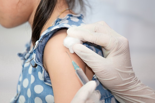 Doctor inyectando la vacunación en el brazo de la niña asiática del niño, concepto sano y médico