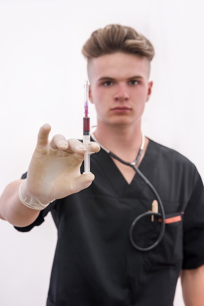 Doctor con jeringa. Joven médico en uniforme médico sosteniendo la jeringa en la mano con guante aislado en blanco