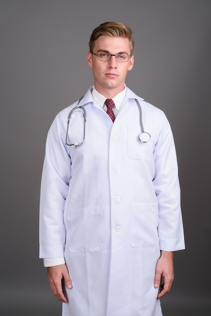 Doctor joven guapo con cabello rubio en la pared gris