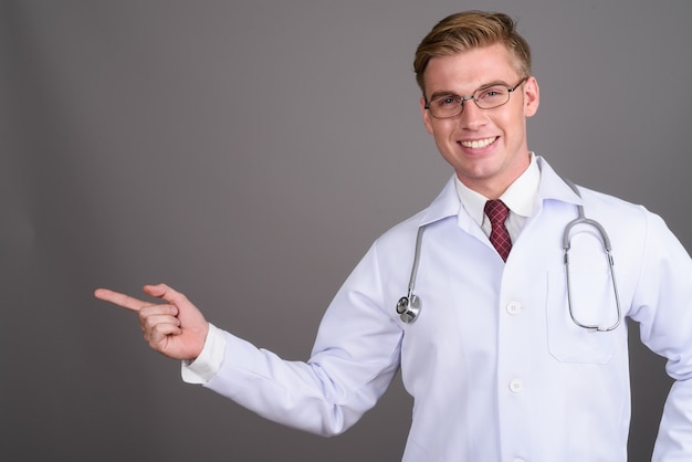 Doctor joven guapo con cabello rubio en la pared gris