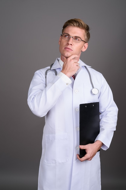 Doctor joven guapo con cabello rubio en la pared gris