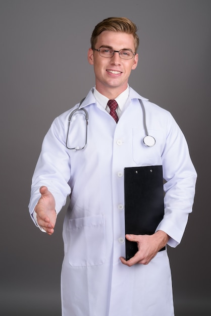 Doctor joven guapo con cabello rubio en la pared gris