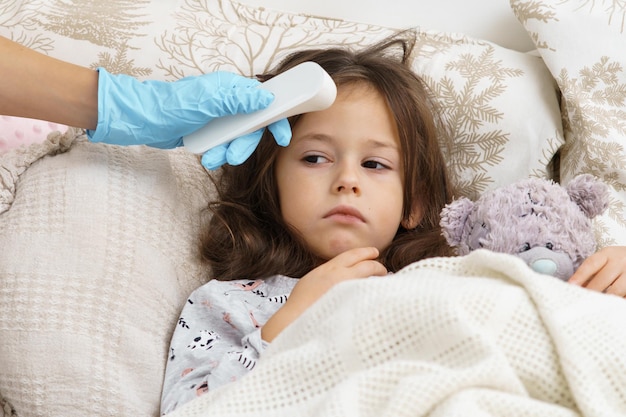 Doctor mano en guante médico medir la temperatura de la niña enferma con termómetro electrónico