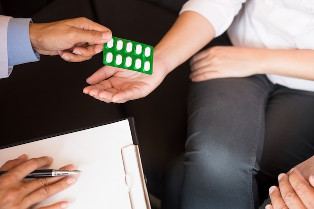 Foto doctor mano sosteniendo la tableta de la droga y explicando al paciente en la habitación del hospital.