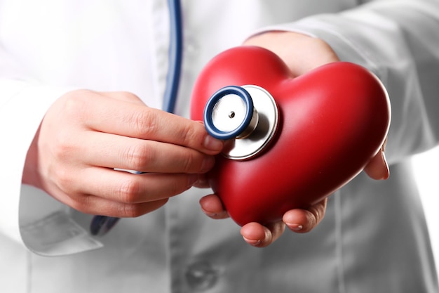 Doctor manos con estetoscopio y primer plano de corazón rojo