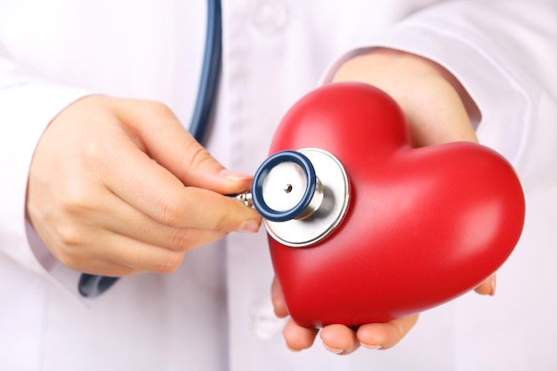 Doctor manos con estetoscopio y primer plano de corazón rojo