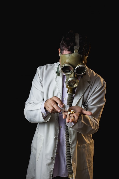 Doctor con máscara de gas tomando pastillas de una botella