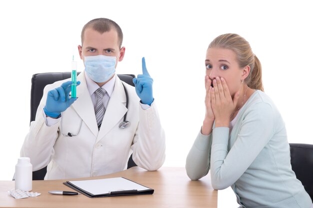 Doctor en máscara con jeringa y paciente aterrorizado aislado sobre fondo blanco.