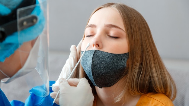 Doctor en máscara médica protectora tomando cultivo nasofaríngeo de prueba de PCR a mujer. Pruebas de diagnóstico pacientes coronavirus covid 19. La enfermera toma una prueba de muestra de saliva a través de la nariz con un hisopo de algodón Banner