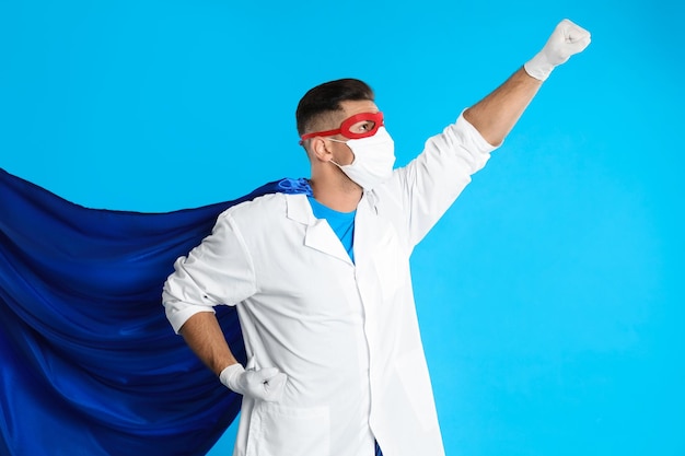 Foto doctor con mascarilla y capa sobre fondo azul claro poder de superhéroe para medicina