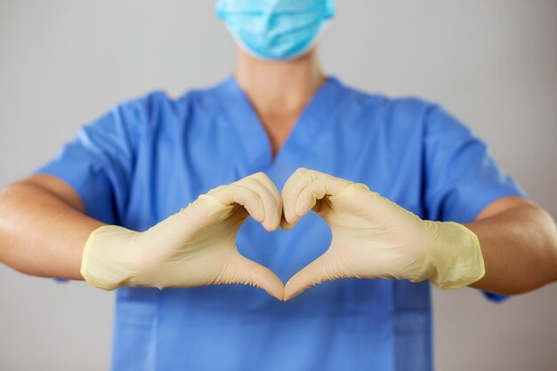 Doctor en una mascarilla y guantes formando un corazón delante de una camisa azul