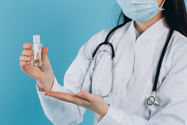 Doctor con mascarilla quirúrgica sosteniendo mostrando botella de bomba de gel de alcohol. Lavarse las manos con gel de alcohol o desinfectante antibacteriano. Covid-19 o concepto de coronavirus.