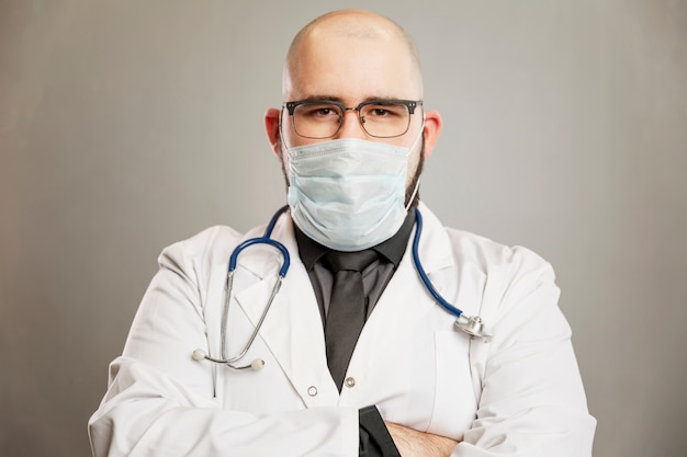 Doctor masculino en una bata blanca y una máscara médica. Pared gris.