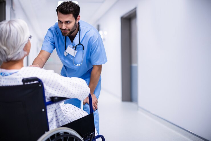 Doctor masculino interactuando con paciente senior en silla de ruedas en el pasillo