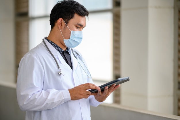 Doctor masculino con una máscara y mirando la tableta