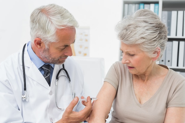 Doctor masculino que inyecta al paciente femenino mayor