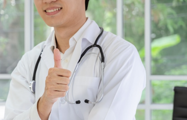 Doctor masculino sonriente en bata blanca mostrando Thumbs up sign