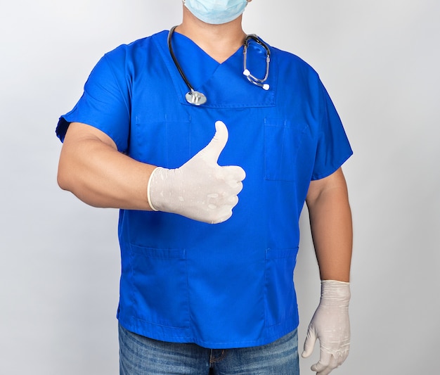 Doctor masculino en uniforme azul y guantes blancos de látex muestra el gesto de la mano derecha como