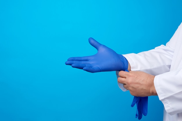 Doctor masculino en uniforme blanco pone en sus manos guantes de látex estériles azules