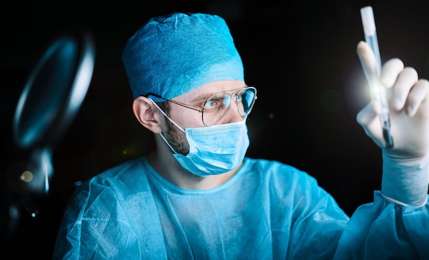 Doctor masculino en uniforme está trabajando con tubos de ensayo médicos en un hospital