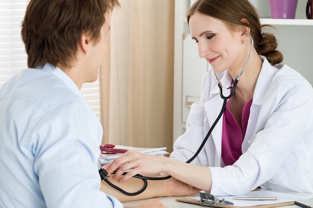 Doctor en medicina femenina sonriente que mide la presión arterial a su paciente masculino. Concepto médico y sanitario