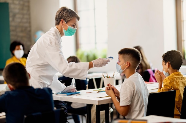 Foto doctor midiendo la temperatura del colegial con termómetro infrarrojo en el aula