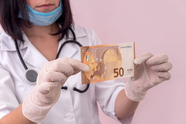 Doctor mirando billete de cincuenta euros sosteniéndolo en guantes