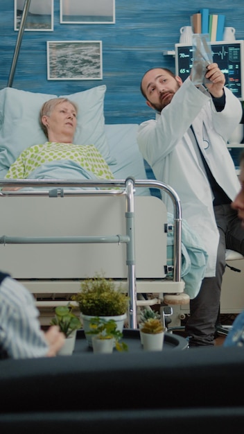 Doctor mostrando escaneo de rayos X a una anciana acostada en la cama del hospital. Médico explicando radiografías a pacientes jubilados con enfermedades para diagnóstico y tratamiento. Adulto mayor enfermo con problemas de salud