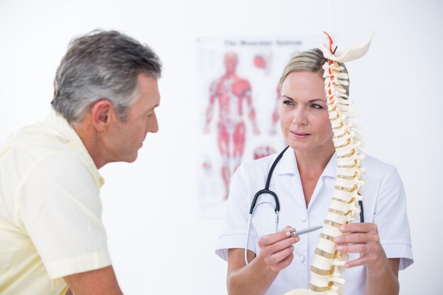 Doctor mostrando a su paciente un modelo de columna vertebral