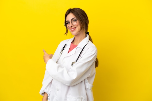 Doctor mujer aislada sobre fondo amarillo apuntando hacia atrás