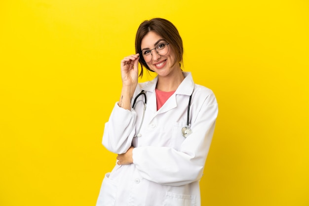 Doctor mujer aislada sobre fondo amarillo con gafas y feliz