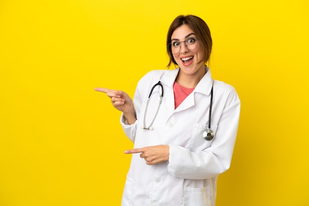 Doctor mujer aislada sobre fondo amarillo sorprendido y apuntando hacia el lado