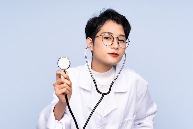 Doctor mujer asiática con estetoscopio sobre pared azul aislado