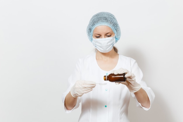 Doctor mujer en mascarilla, sombrero estéril, guantes vierte medicina líquida en una cuchara de botella aislada sobre fondo blanco. Doctora en bata médica. El personal sanitario, la salud, el concepto de medicina.