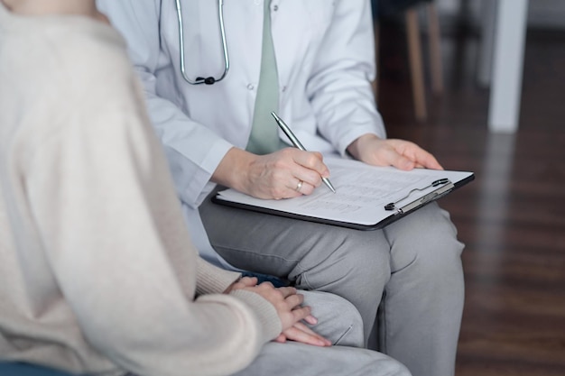 Doctor mujer y niño niño paciente en casa examen médico. El pediatra llenando el formulario médico en el portapapeles, de cerca. Medicina, conceptos sanitarios.